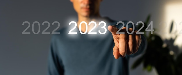 写真 テキストのコピー スペースと灰色の背景に仮想インターフェイスの青い開始 2023 ボタンを押す指。新年のコンセプトです。 2023年の起業を迫るビジネスマン。 2023年の新年の始まり