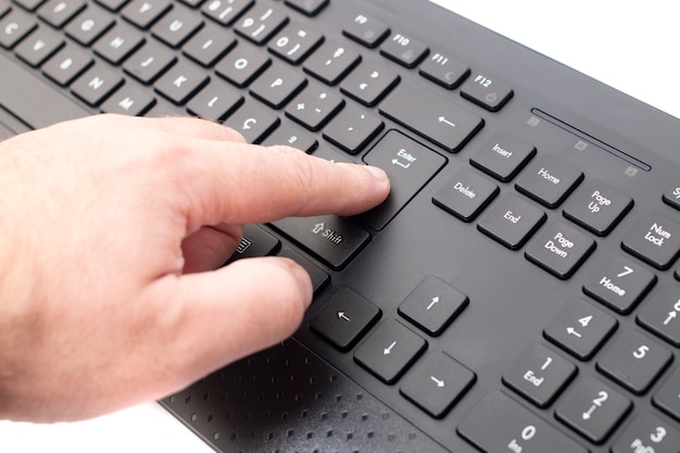 Photo finger pushes enter key on a wireless black personal computer keyboard.