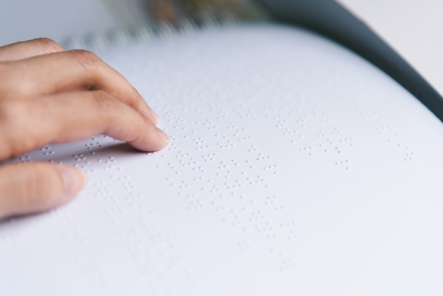 Il dito legge il testo braille in carta bianca.