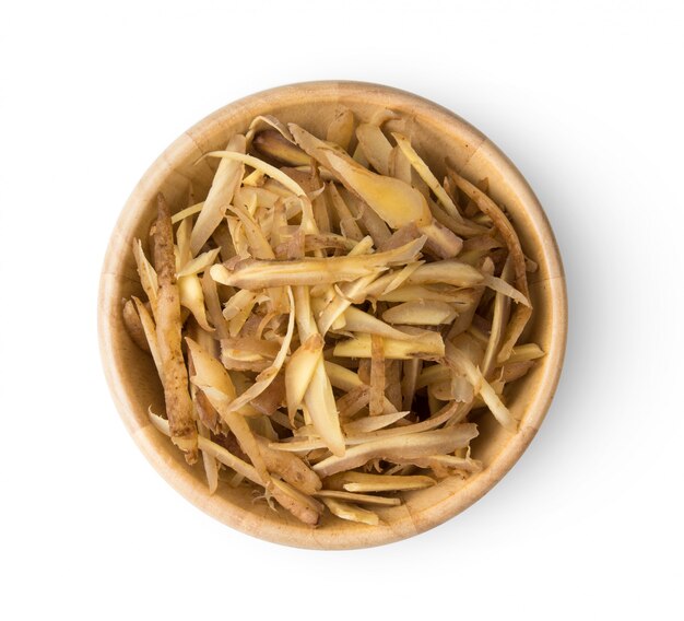 Finger root sliced in wood bowl on white wall.