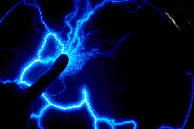 Photo finger touch electric plasma ball on a dark background. static electricity model