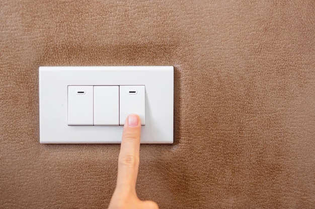 自宅の壁にある照明スイッチを指でオンまたはオフにする省エネ電力の電気およびライフスタイルの概念