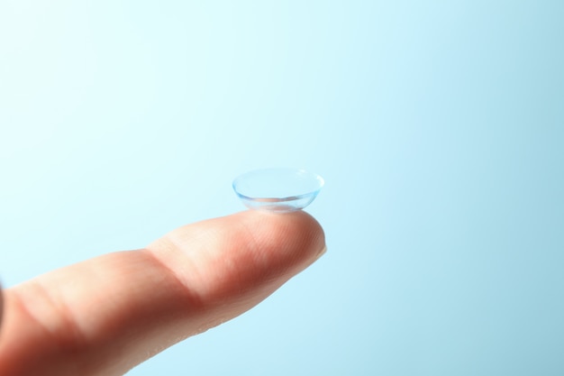 Photo finger with contact lens on blue surface, close up