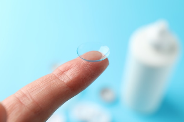 Finger with contact lens on blue surface, close up