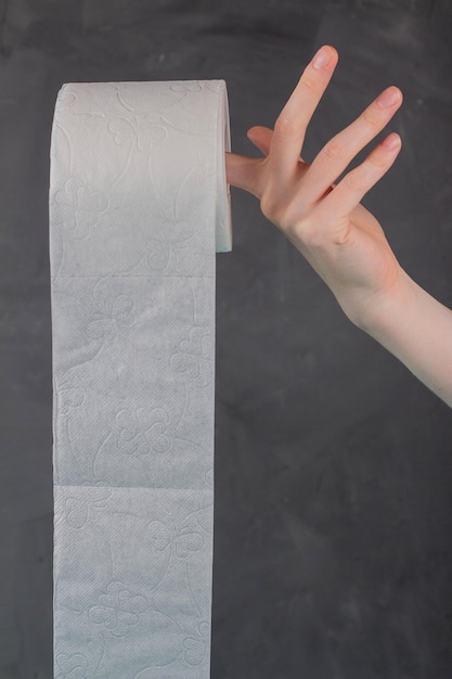 On the finger of a woman\'s hand holding a roll of toilet paper\
on a gray background