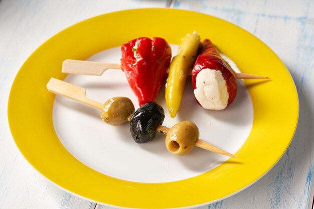 Fingerfood-sticks met olijven en gevulde pepperoni op gele plaat.