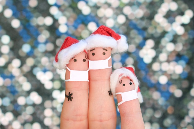 Fingers art of family in medical mask di covid-2019 celebra il natale. concetto di persone in cappelli di capodanno.