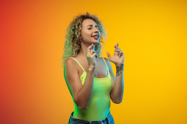 Fingers crossed caucasian young womans portrait on gradient studio background in neon