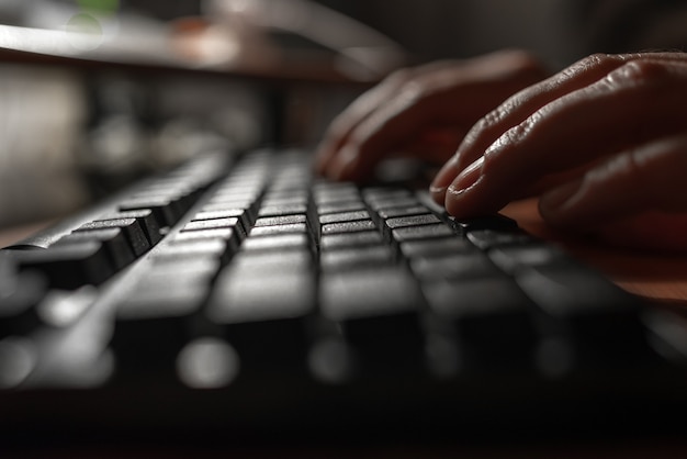 Photo fingers pressing on a computer keyboard in the dark .