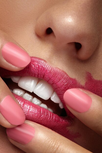 Fingers spreading pink lipstick on mouth in close up photo. Beautiful close up make up