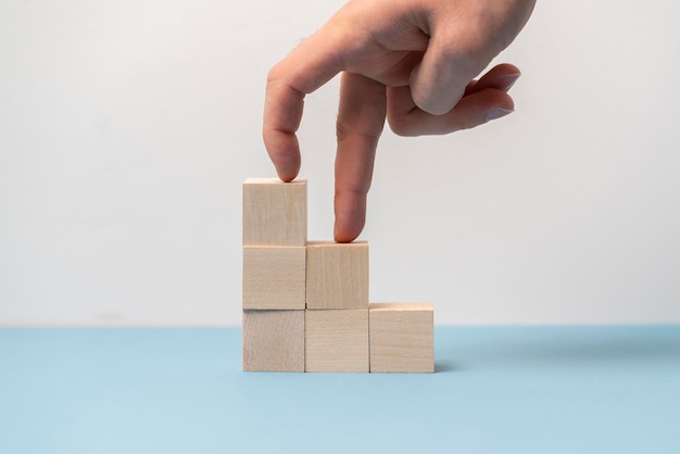 The fingers step on the wooden cubes ladder as symbol of growth