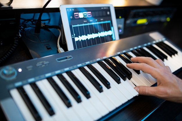 Dita del giovane pianista contemporaneo premendo i tasti della tastiera del pianoforte durante la registrazione di musica dal posto di lavoro in studio