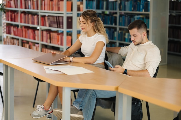 Finish of study in library Female close laptop and take smartphone to relax Man waiting girl Education concept