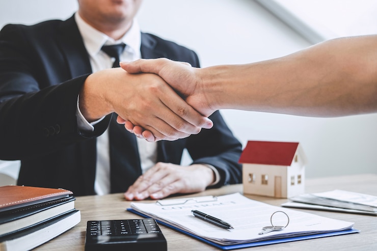 Photo finishing to successful deal of real estate, broker and client shaking hands after signing contract approved application form, concerning mortgage loan offer for and house insurance