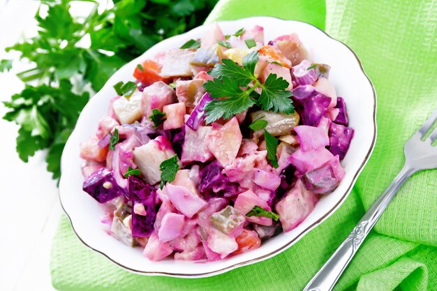 Finnish Rosoli salad with herring, beetroot, potatoes, pickled or pickled cucumbers, carrots, onions and eggs, dressed with mayonnaise in a bowl on white wooden board background