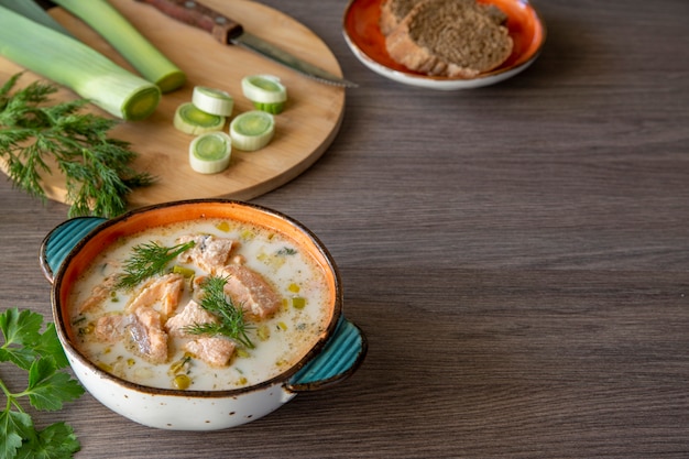 Finnish salmon soup with cream. Fragrant herbs, leek and bread on a wooden table,