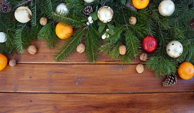 Fir branch and Christmas balls, nuts and tangerines on wooden background