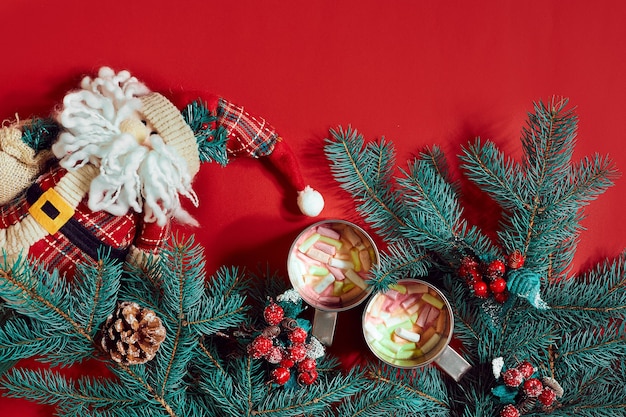 Fir branch, toy Santa and two cups of cocoa with marshmallows on red background. Top view. Flat lay. Copy space. Still life. Christmas and New year