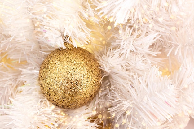 Fir branch with ball and festive lights on the christmas background with golden sparkles
