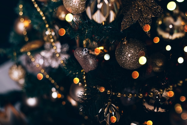 Fir branch with golden balls and festive lights on the dark background with sparkles.