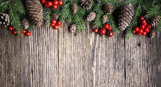 Fir branches, cones and red christmas berries on old wooden board. Christmas composition can be used for border frame background. Top view, copy space