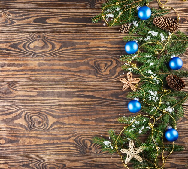 Fir branches decorated with blue Christmas balls cones and a garland on a brown background