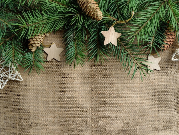 Fir branches, decorated with wooden Christmas decorations, lie on a burlap background with copy space.