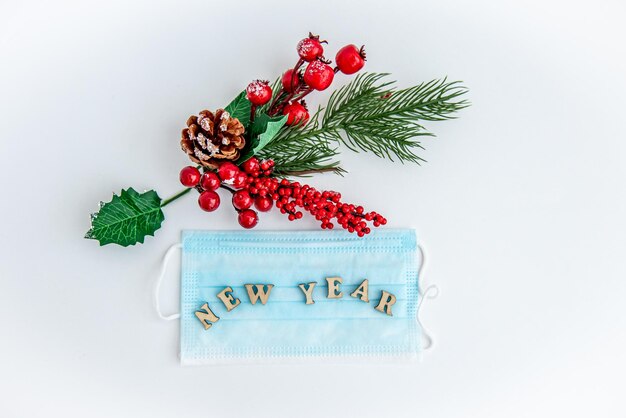 fir branches with red berries and christmas decorations on a white background with a disposablemask