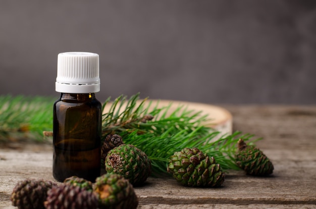 Fir essential oil in the glass bottle with young spruce branches and green cones on a wooden background. Alternative medicine, aromatherapy concept background.