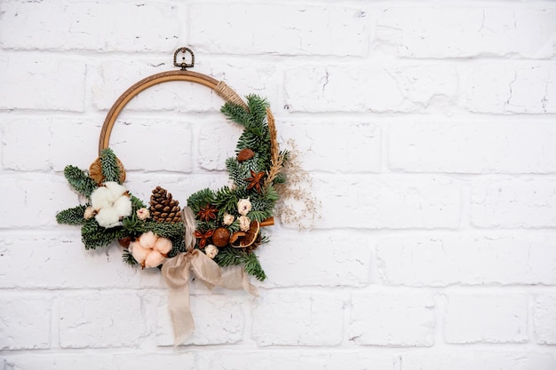 Fir trees decorated with spruce branches and christmas decor hang on a white brick wall space for text