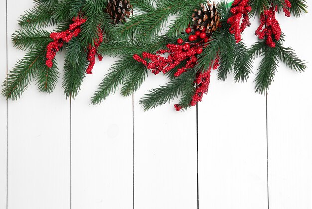 Fir twigs and red berries on light wooden background