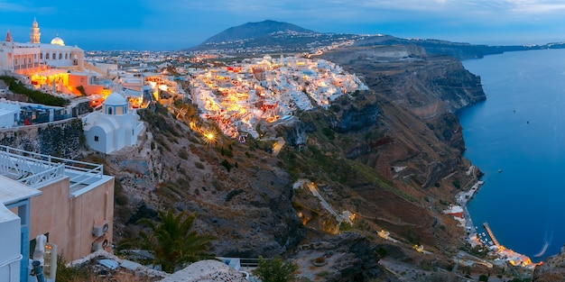 Fira, città principale dell'isola di santorini, mare, case bianche e chiesa durante l'ora blu crepuscolare, grecia