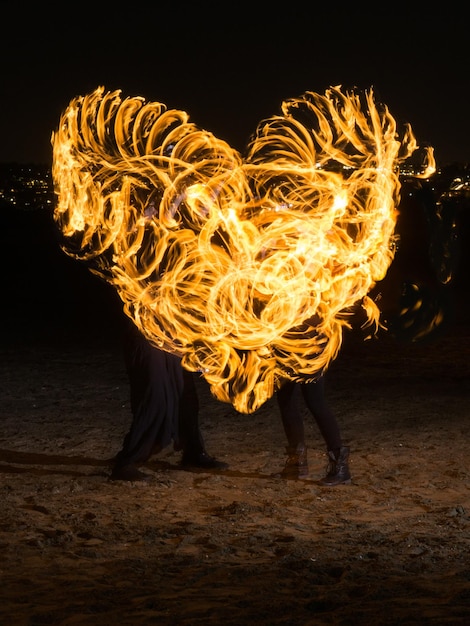 Foto ballerini del fuoco che fanno la forma di un cuore sul campo di notte