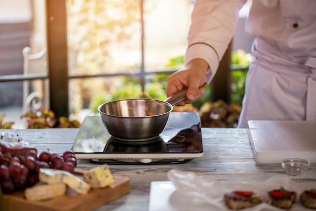 鍋で火をつけます。鍋を持っている男の手。キッチンで働きます。肉のソースを準備します。