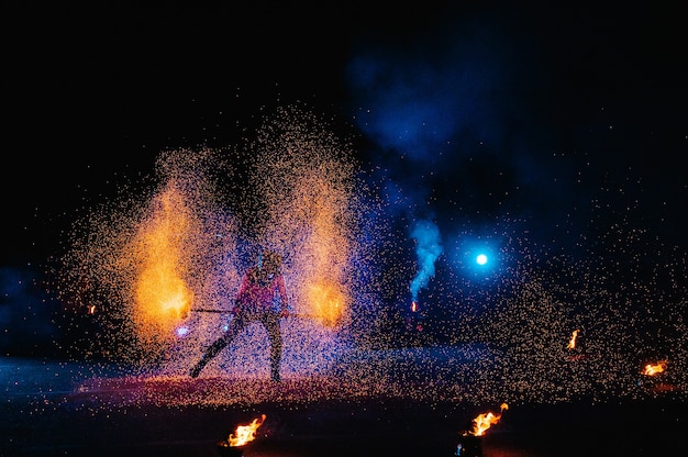 Огненное шоу, танцы с пламенем, мастер-мужчина, жонглирующий фейерверком, выступление на открытом воздухе, рисует огненную фигуру в темноте, яркие искры в ночи. Мужчина в светодиодном костюме танцует с огнем.