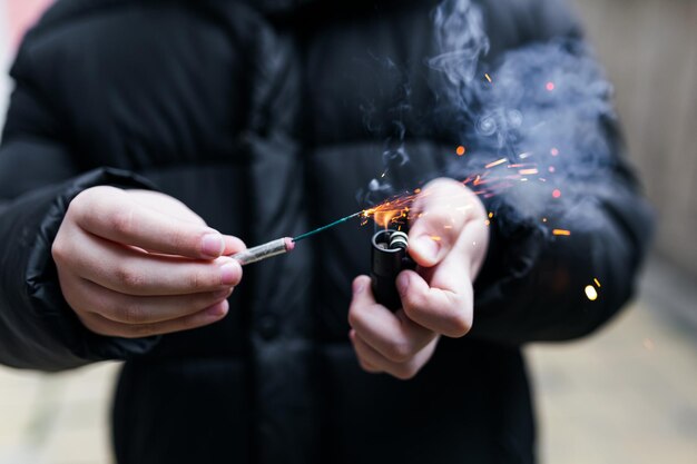 Photo the firecracker in a hand boy holding a burning petard in his hand kid with a pyrotechnics that burns with sparks and smoke outdoors firecracker and lighter in hand