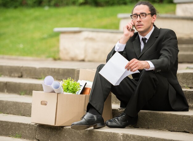 Fired frustrated man in suit sitting near office at stairs.