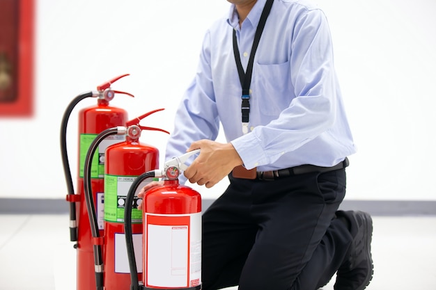 Firefighter checking handle of red fire extinguisher.