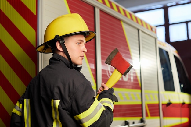 Foto vigile del fuoco completamente equipaggiato con casco e ascia sullo sfondo del camion dei pompieri il soccorritore è pronto a lavorare e aiutare le persone