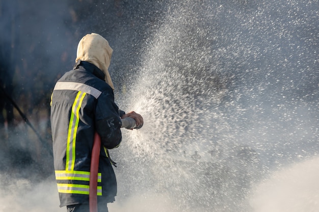 Пожарный распыляет воду из большого водяного шланга, чтобы предотвратить пожар