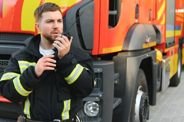 Foto pompiere in uniforme che usa un radio portatile vicino a un camion dei pompieri all'aperto