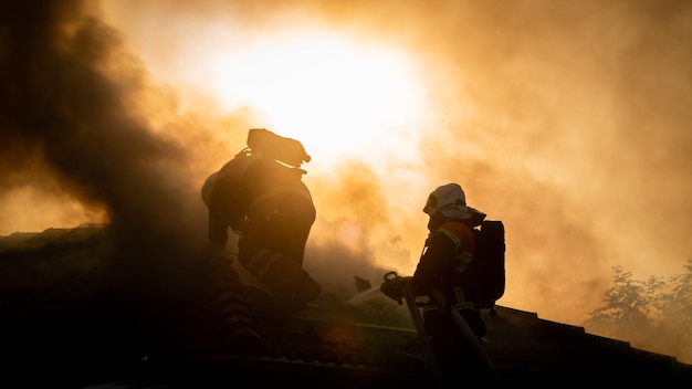 Photo firefighters spraying water on burning roof against sky