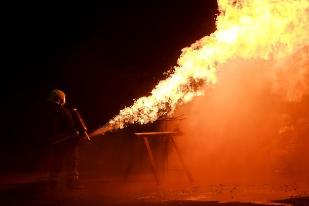 Firefighters wear fire protective clothing to spray fire from\
tanks for nighttime fire drills.