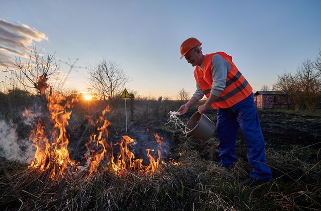 Photo fireman ecologist fighting fire in field in the evening