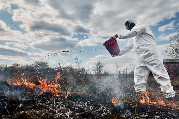 Fireman ecologist fighting fire in field with cloudy sky on background