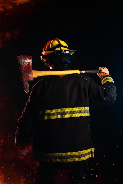 Foto vigile del fuoco sulla schiena che tiene un martello che indossa un'uniforme di protezione speciale sfondo nero notte e fuoco