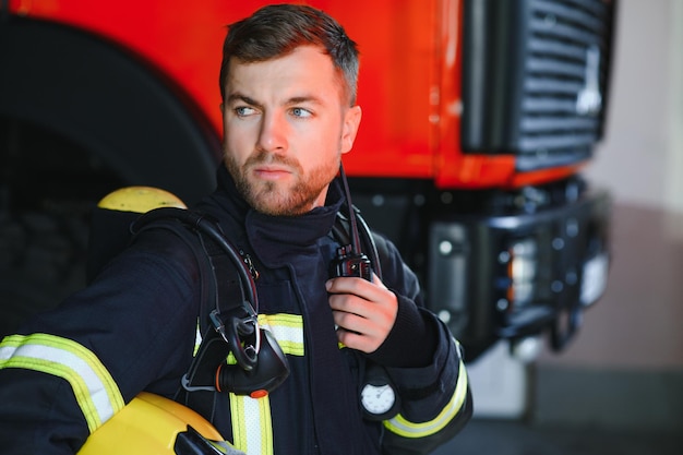 fireman in a protective uniform standing next to a fire truck and talking on the radio