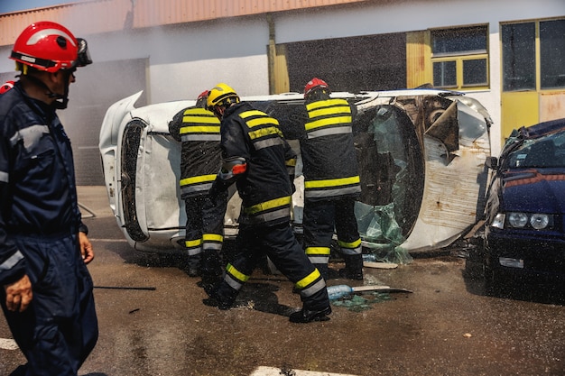 Пожарные в действии. Пожарные тушат пожар и пытаются перевернуть разбившуюся машину в автокатастрофе.