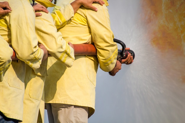 Firemen using water from hose for fire fighting at fire fight training of insurance group. Firefighter wearing a fire suit for safety under the danger training case. 