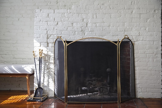 Fireplace with black fire guard screen and tools like shovel and poker. White brick wall